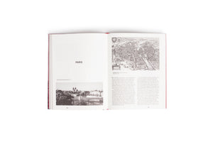 An overhead shot of a red hardcover book laid open on a white surface. The pages feature a chapter on Paris, with German text, a black-and-white photograph of the city, and a detailed historical map from an aerial perspective.