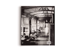 The back cover of a book, featuring a vintage black-and-white photograph of a long, grand library or reading room. Ornate wooden cabinets line the walls, and rows of desks fill the space. The high, arched ceiling is adorned with decorative metalwork featuring silhouettes of monkeys. A block of German text is superimposed on the left side, with a barcode at the bottom right.