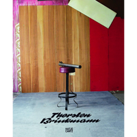An art installation on a book cover for Thorsten Brinkmann. A tall, black metal bar stool with a purple cushioned seat stands on a grey floor. On top of the stool rests a metal tube sculpture resembling a crude cannon. The background is a multi-textured wall with wood paneling, a red section, and a corner with pink paint and floral wallpaper.