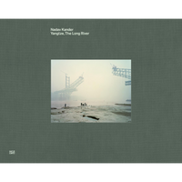 The book cover for Nadav Kander's Yangtze, The Long River, featuring a photograph on a textured gray-green background. The photo depicts a massive bridge under construction, its steel frame disappearing into thick fog over a wide river. On the muddy bank in the foreground, several small human figures are dwarfed by the immense structure.