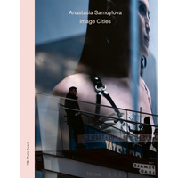 A man on a city escalator is dwarfed by a giant, semi-transparent advertisement of a woman's face and shoulders looming behind him.