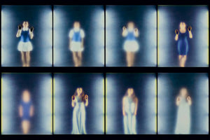 A grid of eight blurry, ethereal photographs of a woman in various blue and white dresses, arranged in two rows. In several frames, she presses her darkened palms against an unseen surface, as if trapped behind glass. The images shift in and out of focus, creating a ghostly and mysterious sequence.