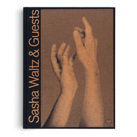 A dark blue hardcover book titled Sasha Waltz & Guests in a vertical, copper-colored font on the spine. The front cover features a large halftone dot image of two hands in the same copper color, with the upper hand's index finger pointing towards the top.