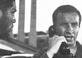 A grainy, black-and-white close-up from the film Preludio 11 (1961), showing a man speaking intently into a telephone receiver. To his left, another man is seen in a dark, shadowed profile.