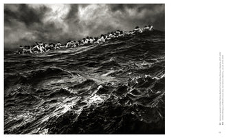 A dramatic black and white photograph showing a long line of people huddled together as they crest a massive, dark wave in a turbulent sea under an ominous, cloudy sky.