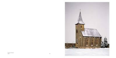 An open book spread with a photograph on the right-hand page showing a detailed model of a quaint, brown church in a snowy landscape. The church has a tall steeple with a cross, a clock on its tower, and its roof is covered in a layer of snow under a flat, white sky.