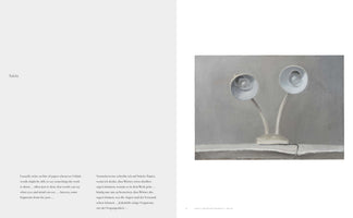 A two-page spread from a book. The left page contains the heading Tafeln above two columns of text in English and German. The right page displays a gray-toned, realistic painting of two white gooseneck desk lamps with round shades, resting on a flat surface against a plain background.