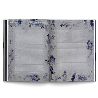 An angled overhead view of an open book on a white surface. The two-page spread features German text arranged in columns, surrounded by numerous sketchy, blue and black ink wash illustrations of human figures in various poses.