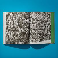 An overhead shot of an open book on a bright blue surface. The pages are filled with a dense collage of hundreds of small, black and white photographs arranged in a grid. The outer edge of the right page has a solid green vertical bar. The book casts a dark shadow below it.