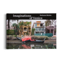 The cover of the art book Imaginations of Venice by Stefanie Bürkle, published by Hatje Cantz. The photograph shows a black gondola with a red cover resting on the muddy bank of a canal. In the background are modern houses, including a large yellow villa and a home under construction, surrounded by palm trees.