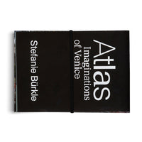 A top-down view of a black book with a black elastic band holding it closed, set against a white background. The cover features white, vertically-oriented text that reads: Atlas Imaginations of Venice, and Stefanie Bürkle.
