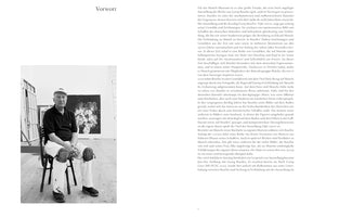 A page from a book with the German title Vorwort. On the left is a black and white photograph of an older artist sitting on a wooden chair in a studio. He wears a cap, a dark polo shirt, and white paint-splattered trousers with kneepads. A large abstract painting hangs on the white wall behind him. On the right side of the page is a column of text in German.