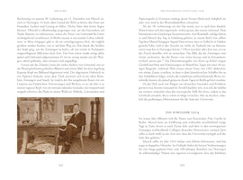 An open book showing two pages of German text, numbered 534 and 535. The left page includes a sepia photograph of a man with a mustache wearing a dark suit, sitting in a cluttered artist's studio. He is at a desk covered with papers, with framed art on the wall behind him and a tall stove to his right.